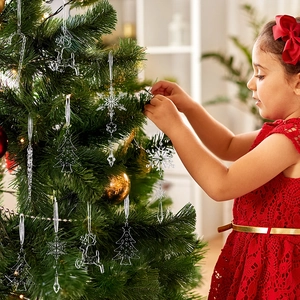 Girl decorating Christmas tree with transparent acrylic snowflake and reindeer pendants