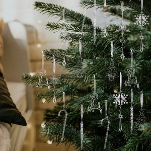 Detailed view of clear acrylic Christmas ornaments hanging on a green tree with warm lights