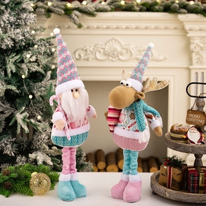 Pink and blue plush Christmas dolls with telescopic legs standing near a cozy fireplace