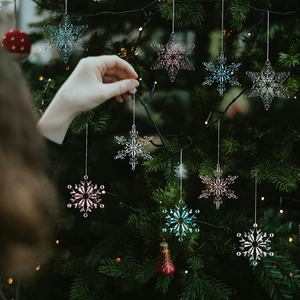 Hand placing clear and pink acrylic snowflake ornaments on a decorated Christmas tree