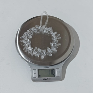 Detalle de corona navideña de acrílico transparente que pesa 11,8 g en una báscula digital
