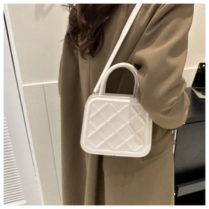 Détail d'un sac à main matelassé blanc porté avec bandoulière sur un manteau en laine