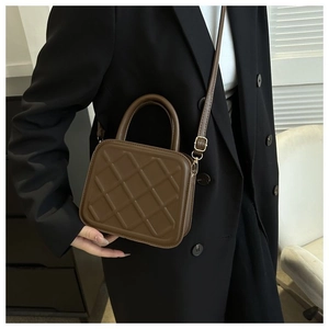 Gros plan d'un sac bandoulière marron matelassé porté sur un mannequin en blazer noir