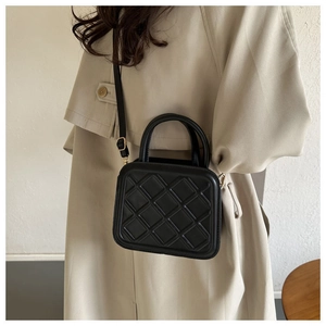Vue latérale du sac bandoulière noir matelassé porté avec un trench-coat beige