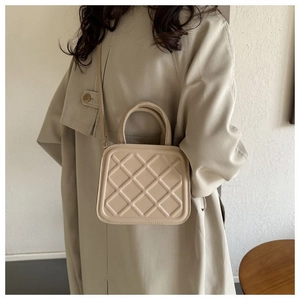 Sac bandoulière beige matelassé avec sangle réglable porté sur un trench-coat classique
