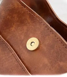 Détail de la boucle magnétique dorée sur un sac bandoulière vintage en cuir marron