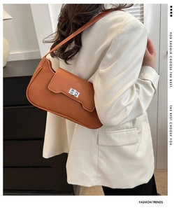 Close-up of caramel leather underarm bag with silver twist lock on white blazer