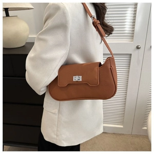 Detailed view of caramel leather shoulder bag with silver clasp on a white blazer