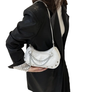 White half-moon crossbody bag with silver chains and studs on a black leather jacket