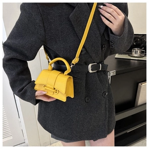 Gelbe Mini-Lederhandtasche mit Ringverschluss, stilvoll präsentiert an einem grauen Anzug