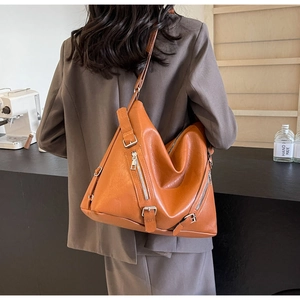 Detail of tan brown leather tote bag featuring decorative zippers and buckle accents