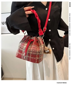 Detail of red plaid wool bucket bag featuring drawstring closure and monster charm