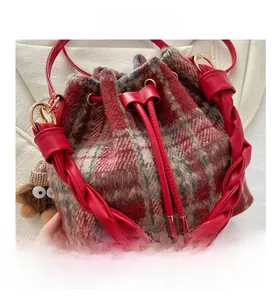 Close-up of wool plaid bucket bag featuring red woven leather handle and owl charm detail