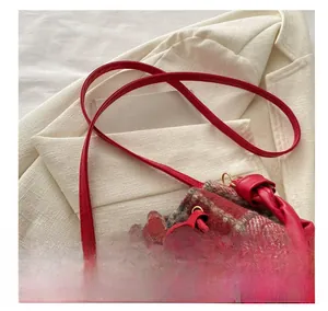 Detail view of red plaid wool bucket bag featuring woven leather strap and drawstring closure