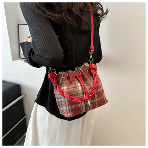 Detail of red and white plaid wool bucket bag with woven leather handle and gold hardware