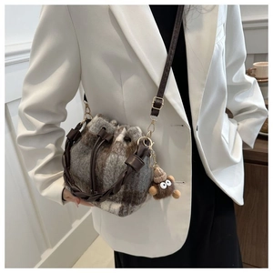 Plaid wool bucket bag with woven handle and plush monkey charm on a white blazer model