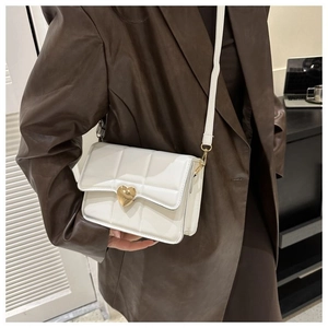 Dettaglio di una borsa a tracolla bianca trapuntata con chiusura a cuore dorata su modella