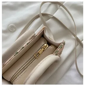 Close-up of smooth gold zipper and floral embroidery details on the cream woven mini bag