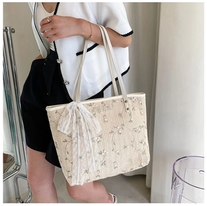 Close-up of straw woven tote bag featuring floral embroidery and white lace bow detail