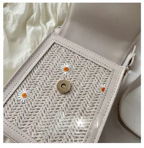 Detailed macro of a woven crossbody bag with magnetic buckle and daisy embroidery