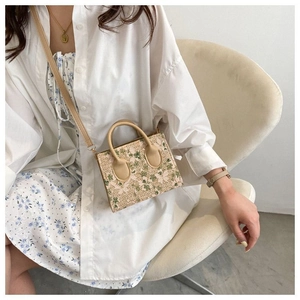 Close-up of woven mini bag with green floral embroidery and light khaki top handles