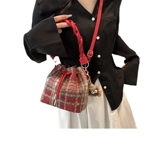 Red plaid wool bucket bag with woven handle and plush charm shown on female model