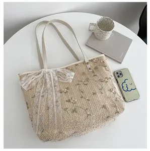 Detail of straw tote bag with floral embroidery and white lace bow on white table