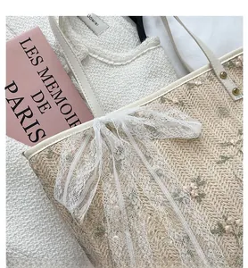 Detail of straw tote bag featuring floral embroidery and a white lace bow detail