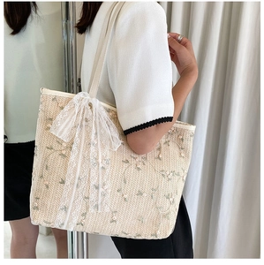Detail of embroidered green vine flowers and lace bow on a beige straw tote bag