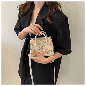 Mini woven handbag with green floral patterns and detachable strap shown by model hand