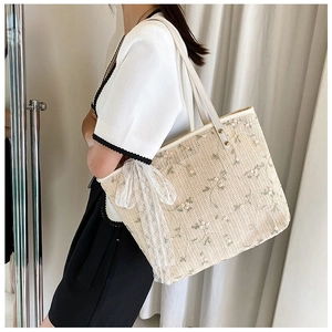 Detail of floral embroidery and lace bow on a cream woven straw tote bag