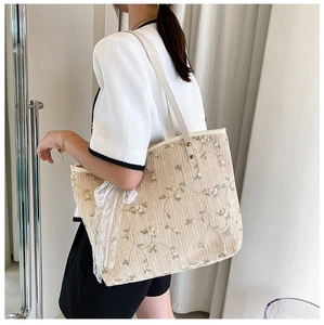 Detail of beige straw tote bag with floral embroidery and white lace bow accessory