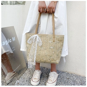 Detail of straw tote bag with floral embroidery and white lace bow decoration