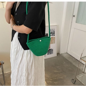 Détail du sac seau tressé vert avec fermoir perle porté par un mannequin femme