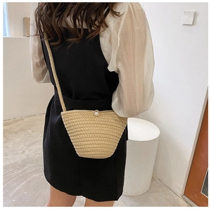Détail du sac seau en paille tissée avec fermoir perle porté à l'épaule par un mannequin