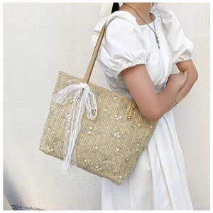 Detail of straw tote bag with floral embroidery and white lace bow decoration
