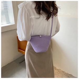 Détail d'un petit sac seau tressé violet avec bouton perle porté en bandoulière