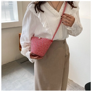 Détail du sac seau tressé rouge et blanc avec boucle en perles et bandoulière sur modèle