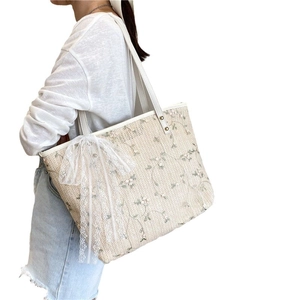 Beige straw tote bag featuring floral embroidery and a large white lace bow detail
