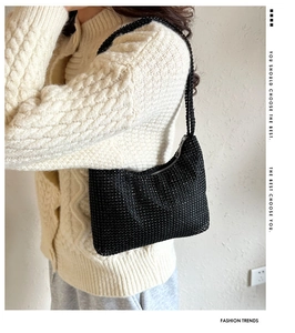 Détail d'un sac baguette noir étincelant avec strass porté à l'épaule sur un pull doux