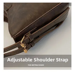 Détail de la bandoulière réglable avec boucles dorées sur un sac seau en cuir marron