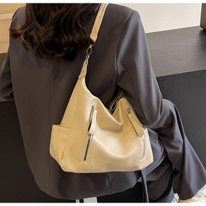 Détail du sac hobo en cuir souple beige avec zips porté sur un blazer gris foncé