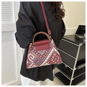 Ethnic woven crossbody bag with geometric patterns, wood handle, and leather straps on model