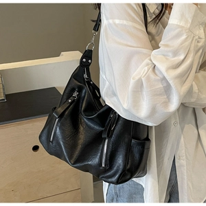 Détail d'un grand sac hobo noir en cuir souple avec zips argentés porté par un mannequin