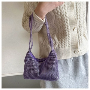 Gros plan du sac baguette à strass violets porté avec un pull en maille blanc cassé