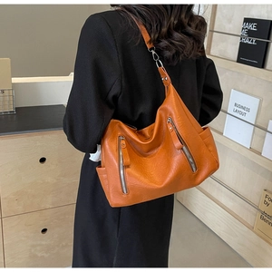 Détail d'un grand sac cabas orange vif avec fermetures éclair argentées porté par un mannequin