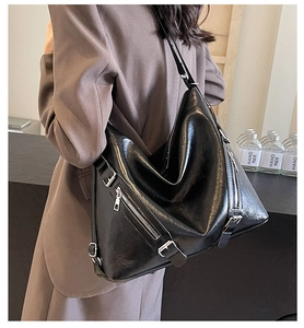 Detail shot of the large black leather bag featuring multiple zipper pockets and metallic buckles