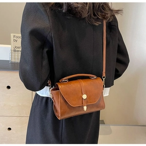 Sac bandoulière rétro marron avec poignée porté par un mannequin en intérieur