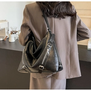 Fashionable black leather shoulder bag with multi-zipper detail in a cafe setting