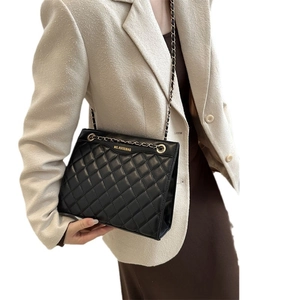 Sac bandoulière matelassé noir avec chaîne porté par un mannequin en veste blanche